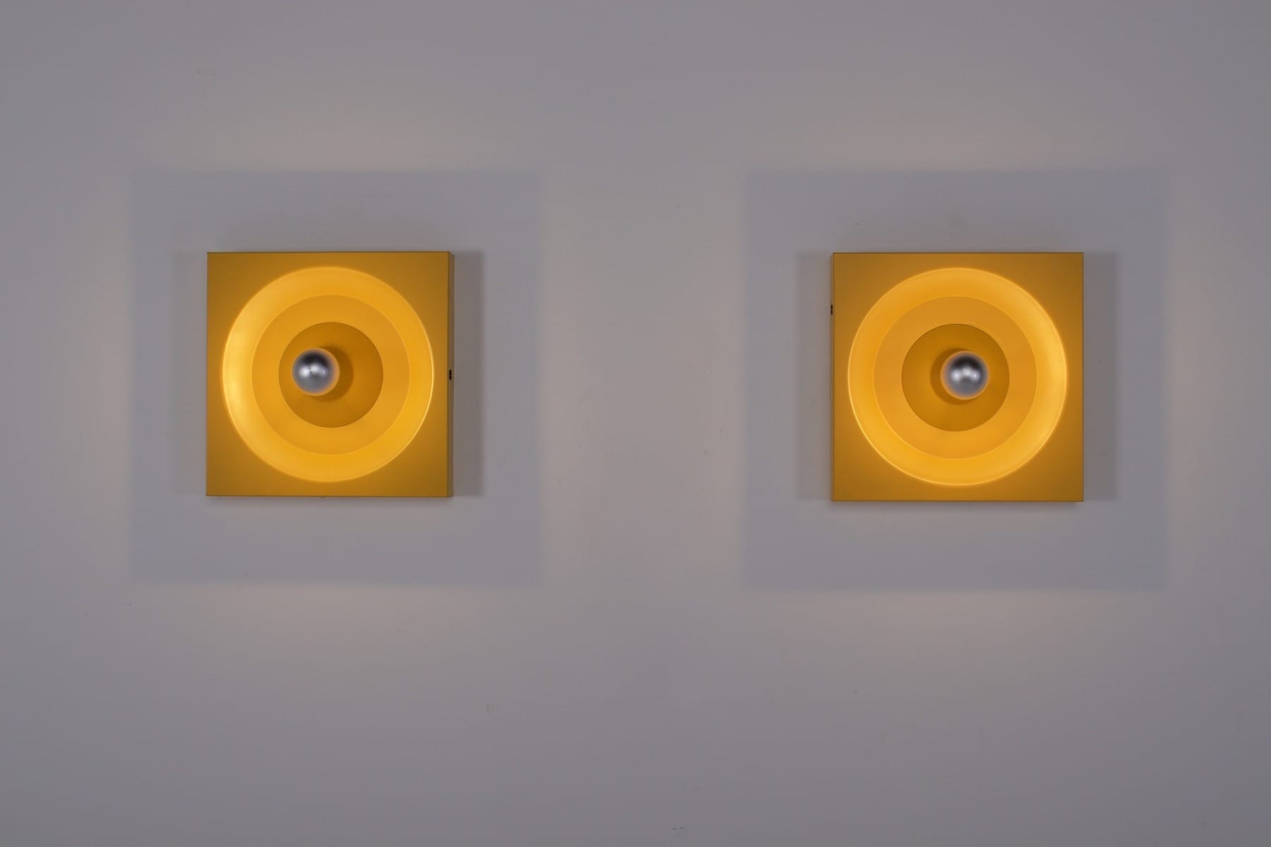 Klaus Hempel per Kaiser, due lampade da parete gialle con lampadine argentate accese.