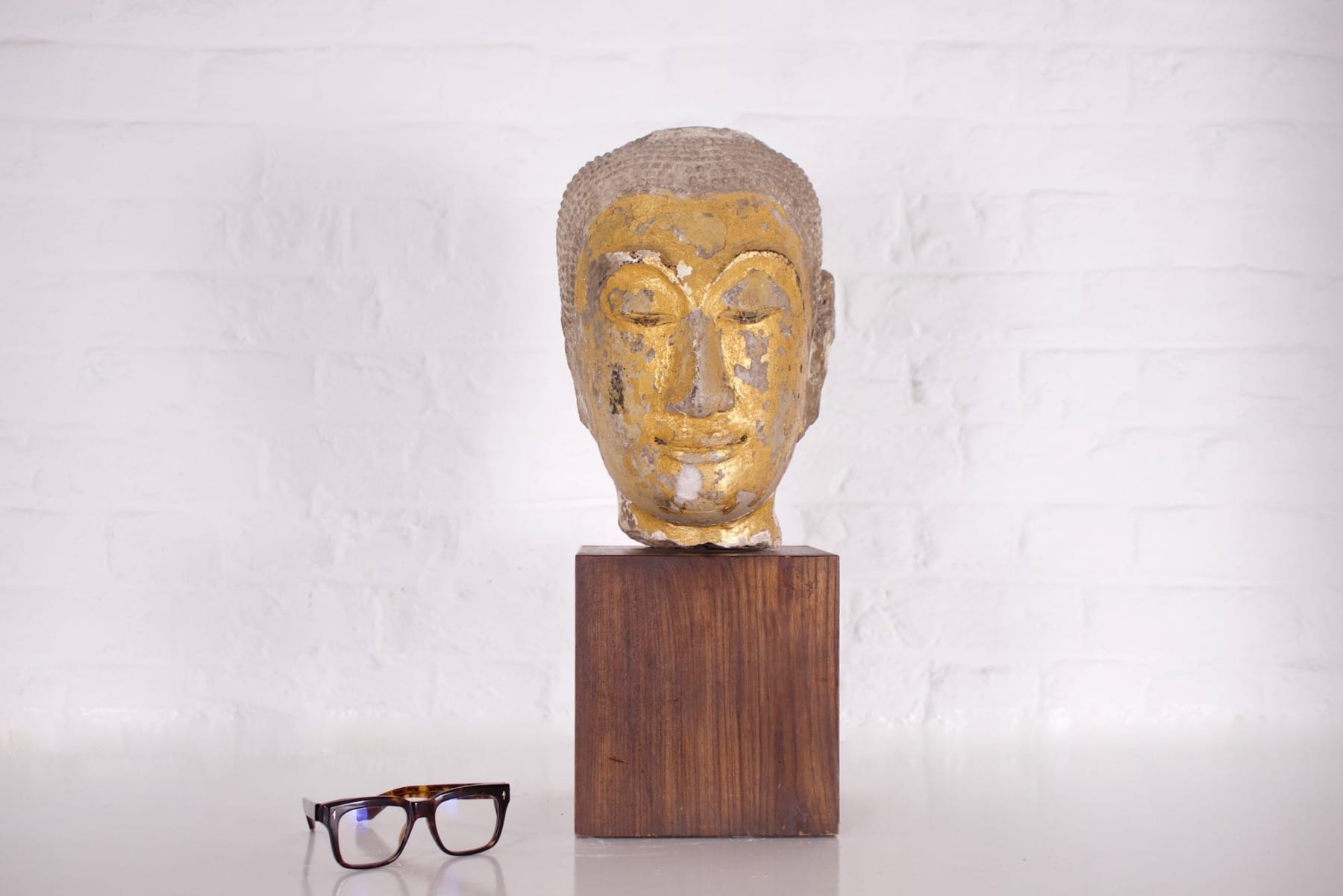 Grande tête en grès doré antique de Bouddha à côté d'une paire de lunettes
