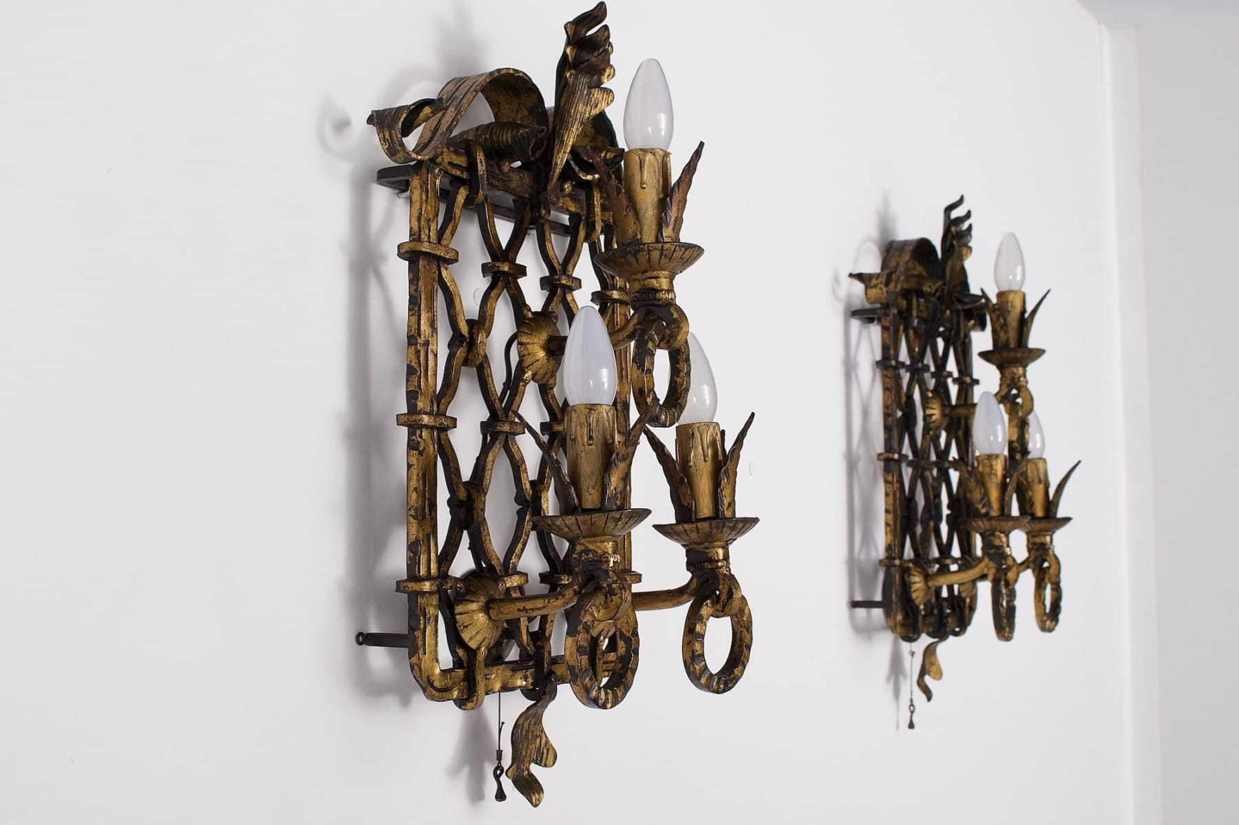 Une paire d'appliques en fer forgé doré néobaroques style Gilbert Poillerat, éteintes et de profil