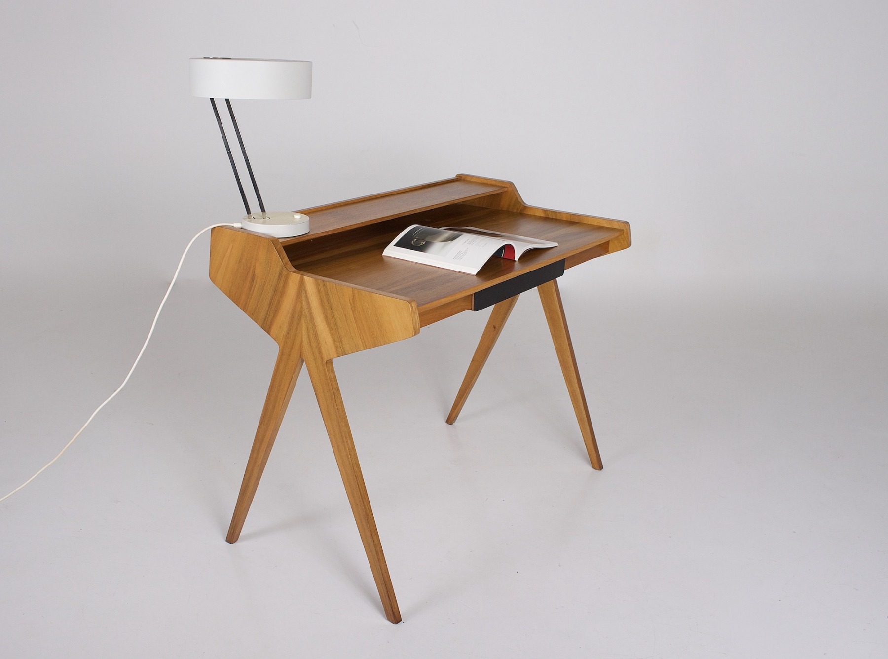 Le bureau en placage de frêne sur lequel est posé une lampe et un magazine