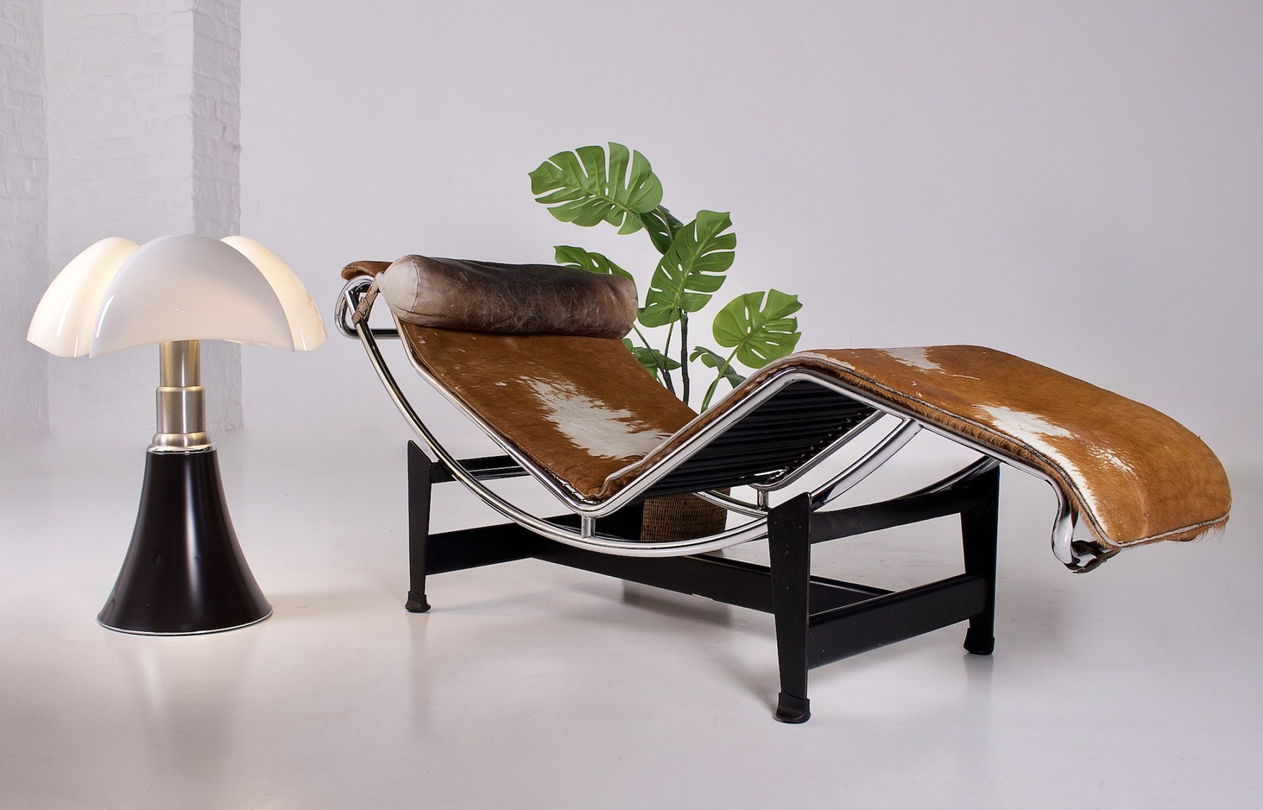 Vue de la chaise longue avec une plante verte, des revues et une lampe pipistrello.
