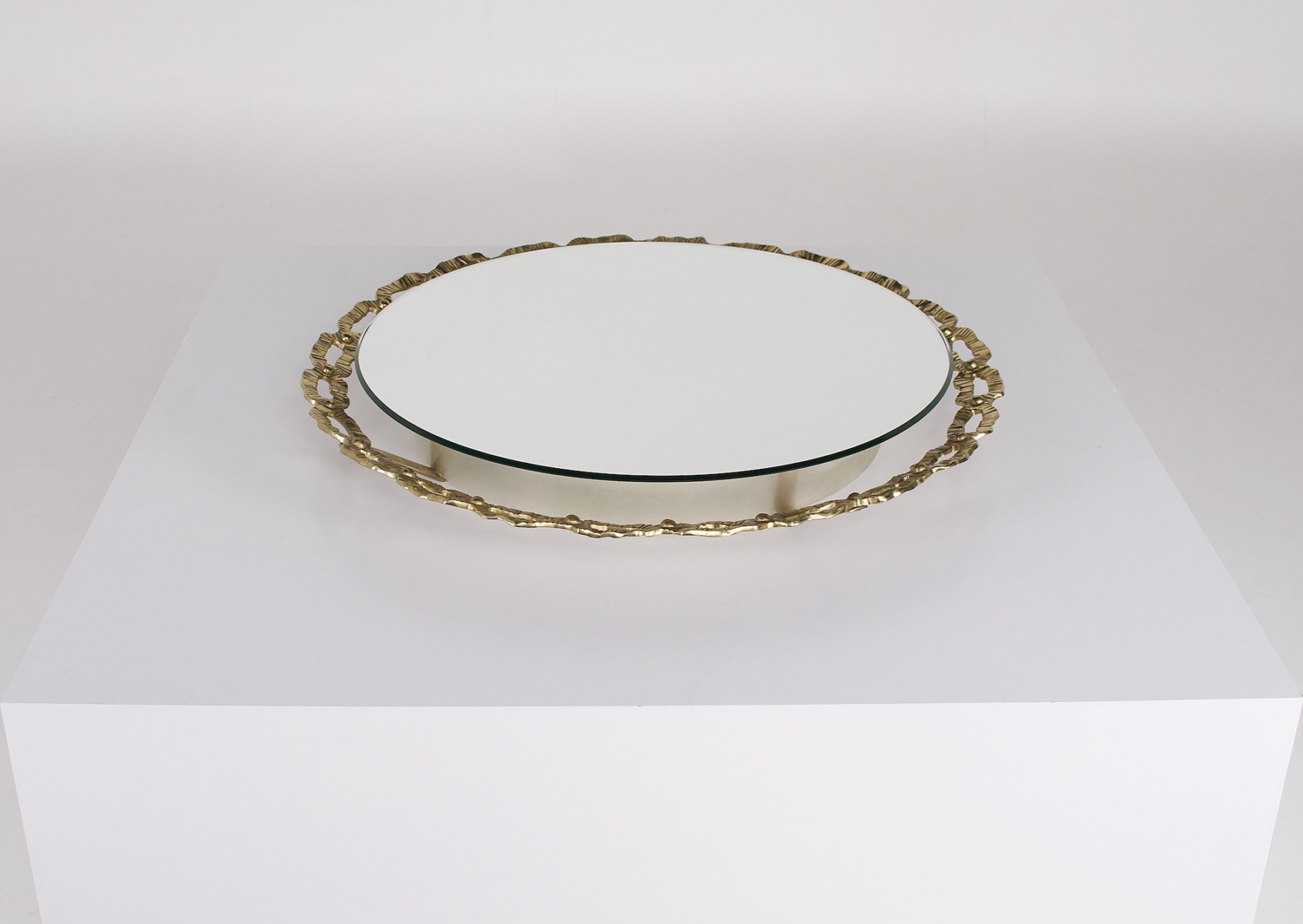 Le miroir lumineux rond en laiton massif, éteint et posé à l'horizontale sur un podium