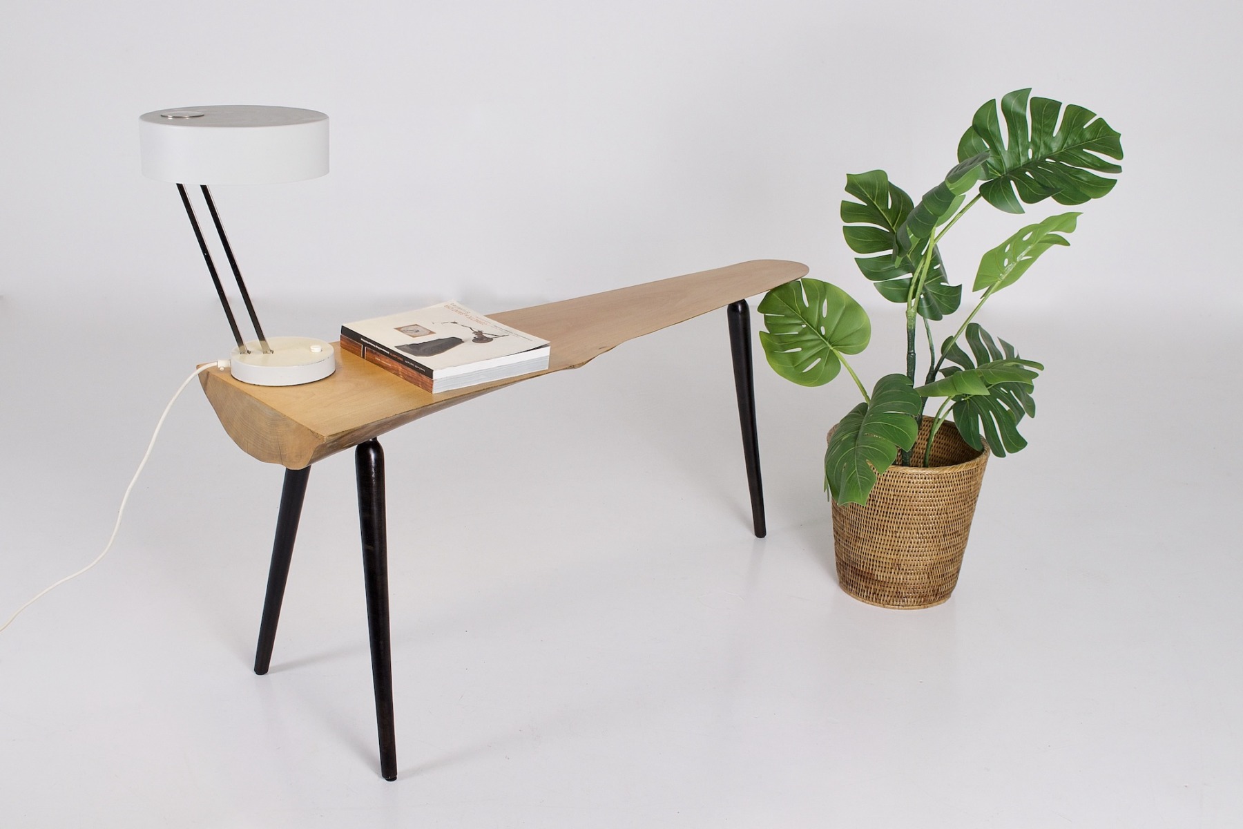 Le petit banc, table basse Wabi Sabi sur laquelle est posée un luminaire et deux magazines, à côté d'une plante