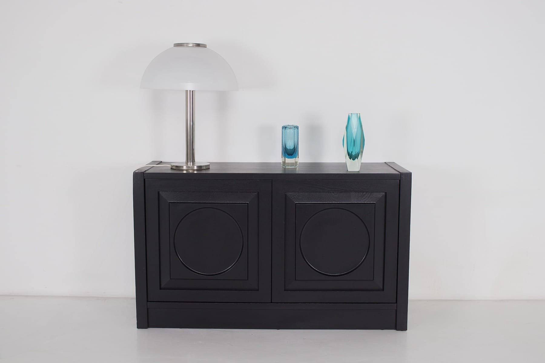 zwart brutalistisch meubel op plint met retro vazen en vintage lamp